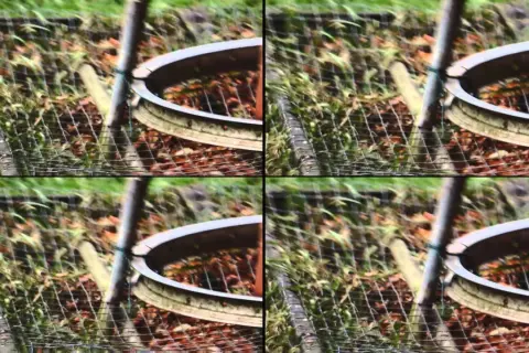 Zniekształcony obraz z efektem rolling shutter, ukazujący fragment ogrodzenia i ziemi.