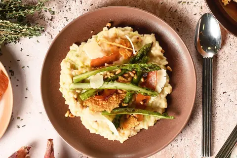 Un crémeux risotto aux asperges vertes, garni de copeaux de parmesan et de fines tranches de prosciutto. Une recette parfaite pour un repas printanier.