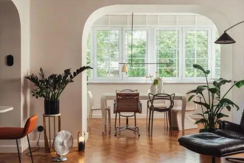 Wnętrze z jadalnią i salonem, gdzie panuje eklektyzm. Widać tu różne style mebli, od nowoczesnych po retro, oraz bogactwo zieleni.