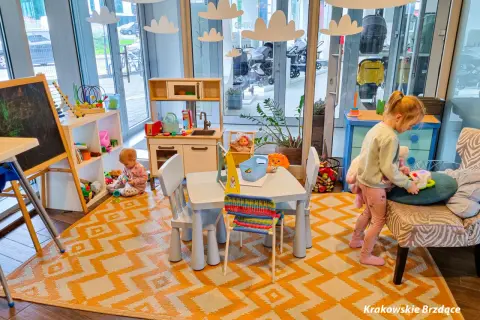 W tej restauracji z kącikiem dla dzieci maluchy bawią się przy stoliku, a obok stoi kuchnia zabawkowa.