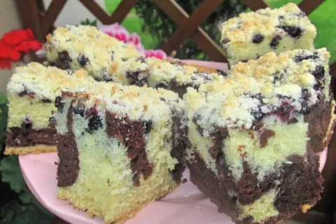 Pyszny biszkopt z jagodami i kruszonką, z czekoladowymi smugami, na różowym talerzu.