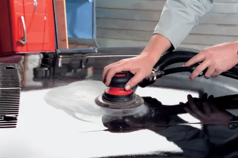 Mani esperte utilizzano una levigatrice per stuccare auto, preparando la carrozzeria per una finitura impeccabile.