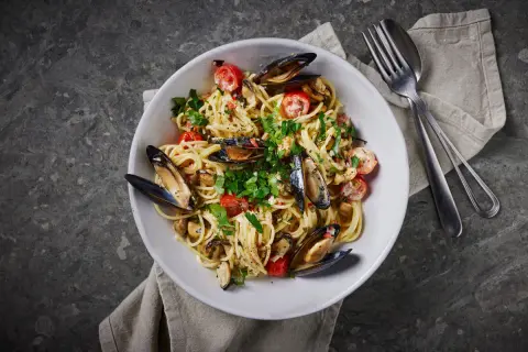 En skål med spaghetti vongole, toppad med färska örter och körsbärstomater. En klassisk italiensk rätt som passar perfekt för en mysig middag.