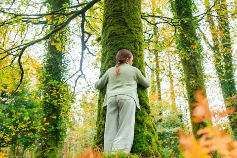 Une jeune fille enlace un arbre couvert de mousse dans une forêt aux couleurs d'automne. La **forêt de rennes** est un lieu magique.