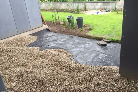 Baustelle für eine splitt terrasse mit Vlies und Kies. Im Hintergrund Rasen und Spielzeug.