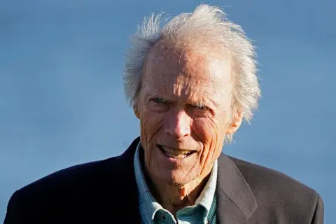 Clint Eastwood heute, mit seinem charakteristischen Lächeln und zerzaust grauem Haar, blickt in die Kamera.
