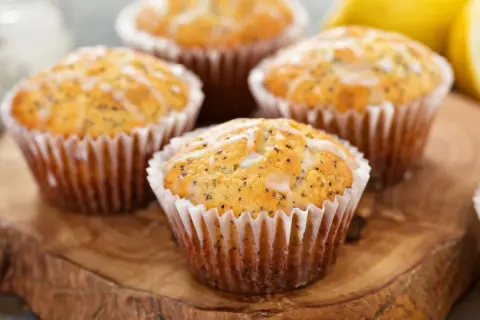 Cztery muffinki cytrynowe na oleju, posypane makiem i polane lukrem, prezentują się apetycznie na drewnianej desce.