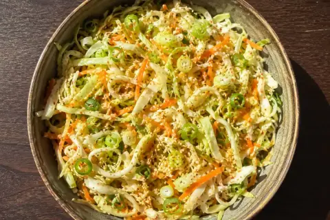 En skål med kålsallad vitkål, morötter och salladslök, toppad med sesamfrön.