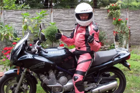 Niska dziewczyna w różowym kombinezonie motocyklowym i kasku siedzi na czarnym motocyklu Yamaha Diversion.