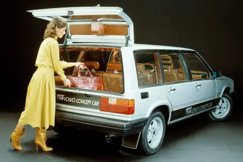 En kvinna i gul klänning lastar en väska i en silverfärgad Volvo concept car från 80-talet.