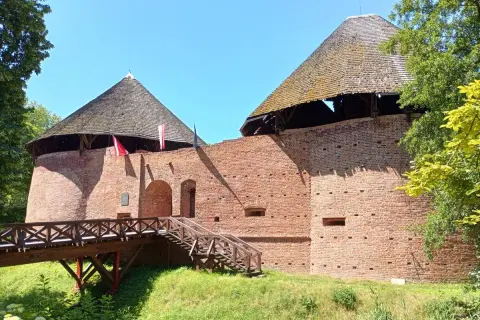 Zamek w Międzyrzeczu, ceglane mury i stożkowe dachy wież. Drewniany most prowadzi do bramy.