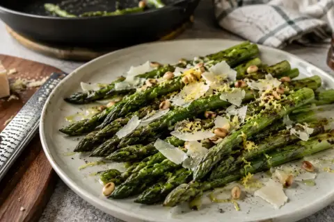 Délicieuse recette d'asperges vertes poêlées, garnies de copeaux de parmesan, de pignons de pin et de zeste de citron. Un plat simple et savoureux.