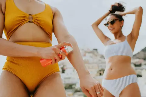 Frau trägt Sonnencreme auf, um sich vor der Sonne zu schützen. Welcher LSF ist wohl der richtige für diesen sonnigen Tag am Strand?
