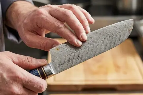 Hände reinigen ein Damastmesser, um Rost von Messer entfernen. Das Muster auf der Klinge ist deutlich sichtbar.
