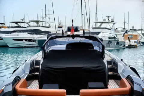Un porto pieno di yacht di lusso, pronti per il trasporto barche. La vista è dal retro di un gommone con sedili in pelle arancione.