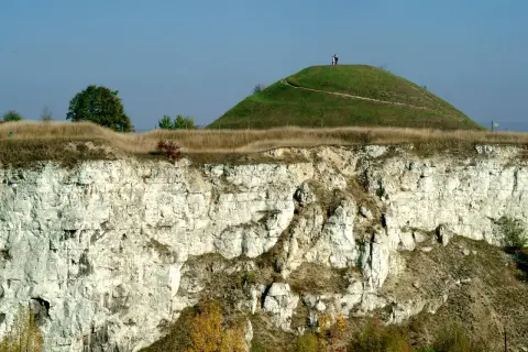 Krakus mound, zielona kopuła z dwiema postaciami na szczycie, góruje nad wapiennym klifem.
