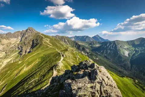 Widok na szlak prowadzący na Kasprowy Wierch. Zielone zbocza Tatr, skaliste szczyty i błękitne niebo z chmurami.