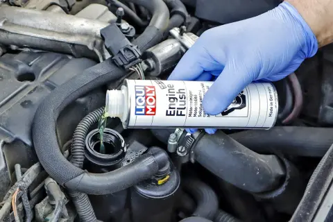 Ręka w niebieskiej rękawiczce wlewa płyn do płukania silnika Liqui Moly. Wiele osób szuka opinii o Ceratec, ale to właśnie ten produkt dba o czystość silnika.