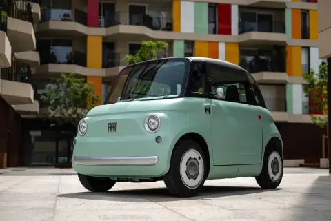 Uroczy, miętowy Fiat Topolino stoi przed kolorowym budynkiem.