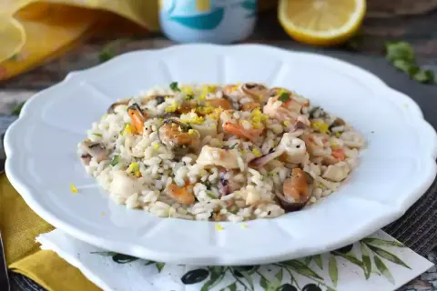 Delicioso risotto de marisco con mejillones, gambas y calamares, adornado con ralladura de limón y perejil fresco.