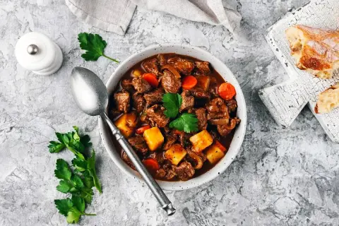 En mustig boeuf bourguignon med möra köttbitar, potatis och morötter i en rik vinbaserad sås. Serveras med en skiva rustikt bröd.