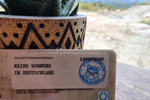Dokument mit "Keine Wohnung in Deutschland" und einem Stempel. Ein Sukkulent in einem Topf steht daneben. So kann man dauerhaft reisend melden.