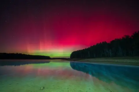 Vibrant pink and green aurora borealis reflected in a calm lake. This scene captures the magic of how to take pictures of northern lights.
