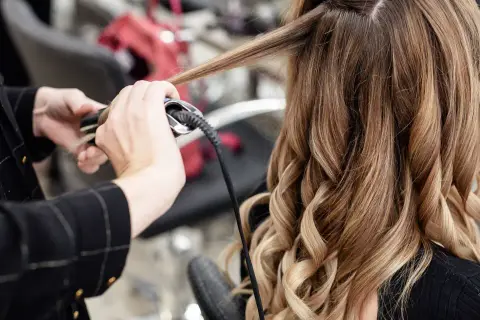 Manos expertas usando una tenaza para rizar el cabello rubio y castaño, creando ondas perfectas.