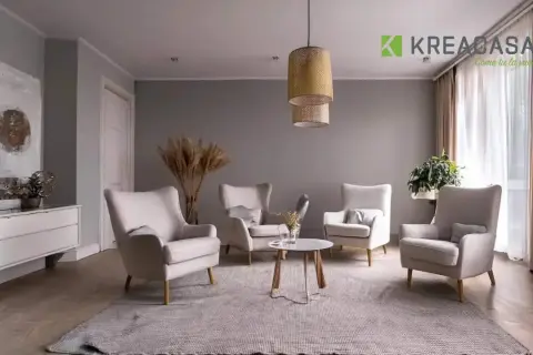 Salotto accogliente con poltrone color ecru, tappeto grigio e un tavolino centrale. Pareti grigie e tende color tortora completano l'arredo.