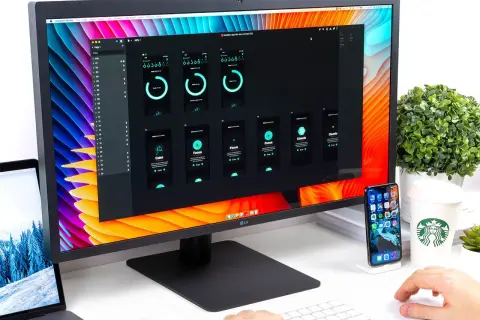 Na monitorze widać projekt aplikacji mobilnej, a obok leży laptop z otwartą **matrycą w laptopie**.