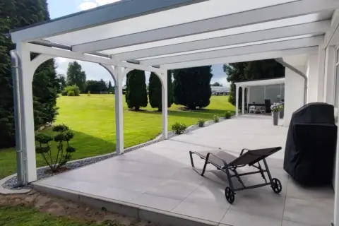 Modernes Terrassendach bauen: Ein Liegestuhl und Grill warten auf sonnige Tage unter dem neuen Dach. Der Garten lädt zum Entspannen ein.