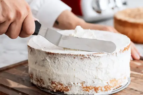 En hand sprider fluffig grädde på en tårta. Ett perfekt tårta recept att följa!