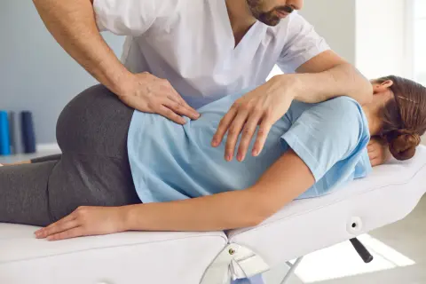 Ein Therapeut behandelt einen Beckenschiefstand. Er legt seine Hände auf den Rücken einer liegenden Person, um eine Korrektur vorzunehmen.