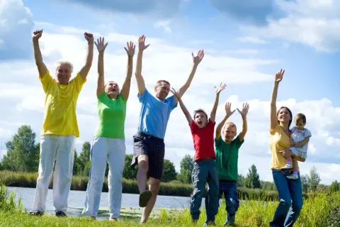 Familia disfrutando de actividades al aire libre, saltando y riendo junto a un lago.
