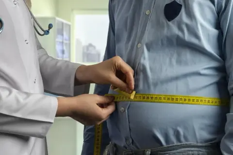 Un médecin mesure le tour de taille d'un homme. Une femme de 50 ans pourrait avoir un tour de taille similaire.