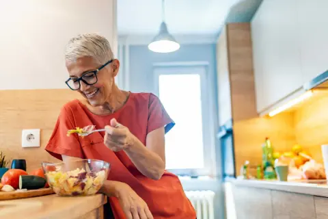 Femme souriante de 50 ans savoure une salade fraîche. Une alimentation saine pour maîtriser les calories.