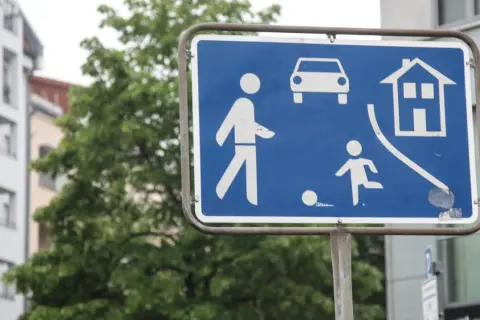 Zeichen 325.1: Fußgängerzone mit spielenden Kindern und Autos. Ein Haus symbolisiert Wohngebiet.