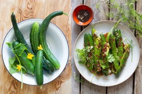 Färska gurkor i en skål och en tallrik med kryddig asiatisk gurksallad, garnerad med örter och blommor.