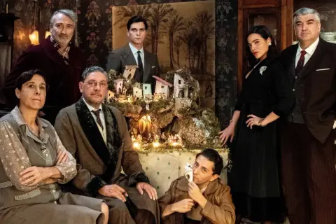Il cast del film "Natale in casa Cupiello" posa davanti a un presepe illuminato.
