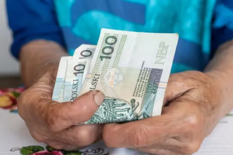 Dłonie trzymają polskie banknoty 100 zł. Czekamy na informacje, kiedy będzie wypłacana trzynastka.