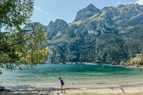 Chłopiec bawi się na plaży nad Jeziorem Garda, w tle góry. Idealne pola kempingowe czekają na odkrycie.