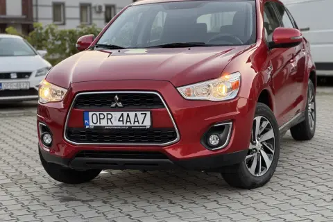 Czerwony Mitsubishi ASX 1.6 benzyna z tablicą rejestracyjną OPR 4AA7 zaparkowany na kostce brukowej.