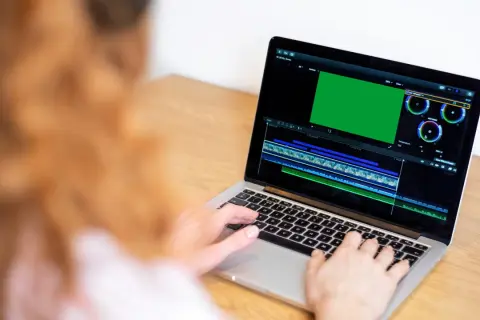 Osoba pracuje na laptopie, edytując wideo. Na ekranie widać zielony podgląd i oś czasu, co sugeruje, że uczy się, jak nagrywać ekran na laptopie.