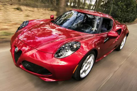 Czerwone Alfa Romeo 4C z połyskiem lakieru perłowy a metalik, pędzące przez las.