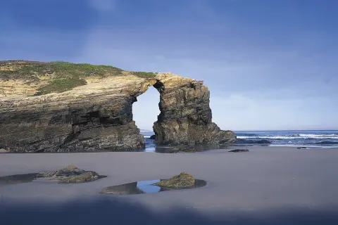 Arco natural en la costa de Ribadeo, con el mar y el cielo azul de fondo.