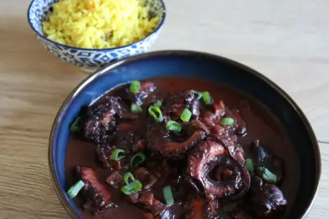 Un plat de daube de poulpe savoureux, garni de ciboule fraîche, servi avec du riz jaune parfumé.