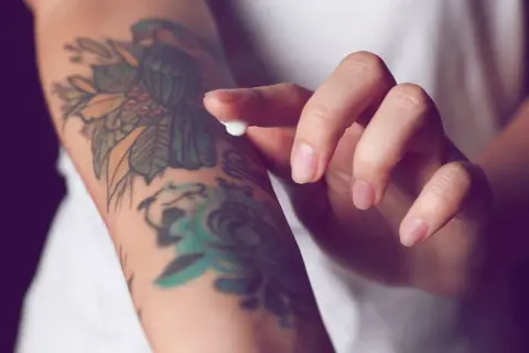 Hand testet Tattoo-Creme auf einem bunten Arm-Tattoo.