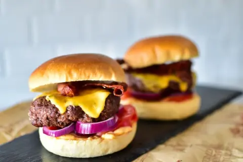 Zwei saftige Burger mit geschmolzenem Käse, knusprigem Speck und roten Zwiebelringen. Die Burger patties sind perfekt gegrillt.