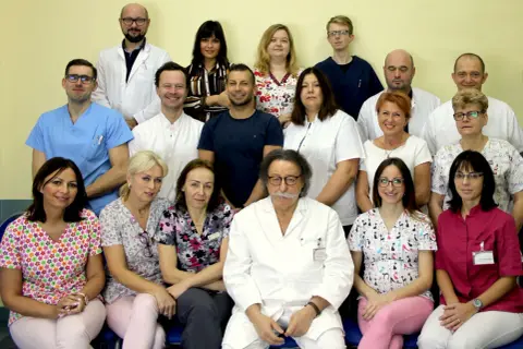 Grupa lekarzy i pielęgniarek w białych fartuchach i kolorowych strojach medycznych pozuje do zdjęcia.