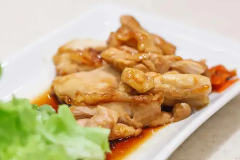 Straccetti di pollo succulenti e dorati, serviti su un piatto bianco con insalata fresca e carote sottaceto.